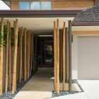 Modern house entrance with bamboo poles and greenery on both sides.